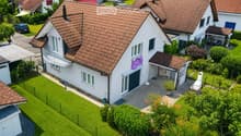 A two-story house with a red-tiled roof, white exterior, and a well-maintained garden with a barbecue and seating area.