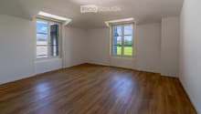 Empty room with wooden flooring, white walls, and large windows offering a view of the outdoors.