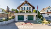 A two-story house with a modern design, featuring a garage, balcony, and well-maintained garden.