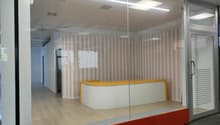 Modern office space with a reception desk, glass partitions, and striped wallpaper in the background.