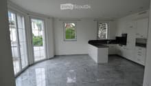 Modern kitchen with white cabinets, black countertop, marble flooring, and large windows letting in natural light.