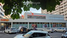 Modern building with large windows and a 'coop' sign, surrounded by parked cars and pedestrians.