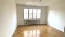 Empty room with wooden floor, white walls, windows with radiators, no furniture
