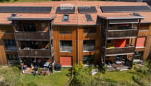 Modern multi-story building with wooden balconies, solar panels on the roof, and a landscaped garden area.
