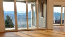 Empty room with wooden flooring and large sliding glass doors leading to a balcony with a scenic view.