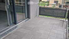 Modern balcony with large grey tiles, glass sliding door, metal railing, and view of neighboring houses.