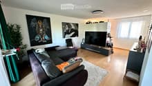 Modern living room with a dark grey sectional sofa, coffee table, flat-screen TV, and decorative artwork on the walls.