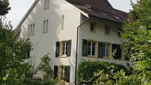 Two-story white house with a brown tiled roof, multiple windows with shutters, and a well-maintained garden in front.