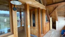 Wooden hallway with large windows, exposed wooden beams, and a modern wall-mounted light fixture.