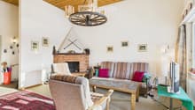 Cozy living room with a fireplace, patterned sofa, wooden coffee table, armchair, television, and decorative picture frames on the walls.