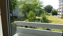 Balcony with white railing, overlooking a green park area with trees and a building in the background.