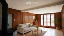 Modern living room with wooden walls and floor, large sliding glass doors leading to a balcony, a light-colored sofa, a wooden coffee table, and decorative plants.