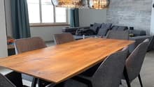 Modern dining area with a wooden table, six grey chairs, a grey sofa, and two pendant lights hanging from the ceiling.