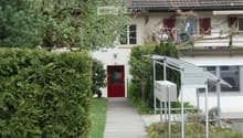 2 story house, brown roof, red door, white walls, hedges, walkway, mailbox