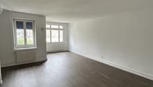 Empty room with wooden flooring, white walls, and large windows with radiators below them.