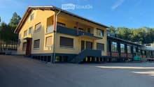 Two-story yellow building with a raised ground floor, multiple windows, and a balcony on the upper level.