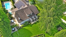 Aerial view of a house with a well-maintained garden, swimming pool, patio furniture, and a covered outdoor seating area.