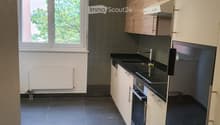 Modern kitchen with white and wood cabinets, black countertops, and stainless steel appliances. Features a window with a view of greenery.