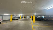 Underground parking area with several parked cars, yellow pillars, and marked parking spaces.
