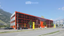 Modern, multi-story building with orange and black facade, large glass windows, and a parking area with several cars.