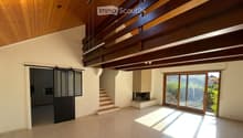 Open-plan living space with wooden ceiling beams, large sliding glass doors leading to a balcony, staircase, and fireplace.