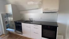 Modern kitchen with white cabinets, black countertops, stainless steel appliances, and wooden flooring.