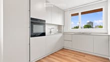 Modern kitchen with white cabinets, wooden flooring, and a large window overlooking a cityscape.