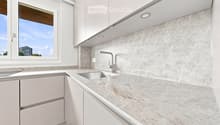 Modern kitchen with white cabinets, marble countertop, and a stainless steel sink with a modern faucet. The backsplash features a textured, light-colored tile design.
