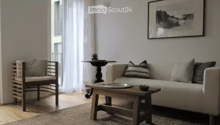 Modern living room with white walls, wooden floor, large windows, balcony access, sofa, coffee table, chair, small table, and picture frame.