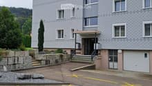 Gray building, multiple windows, garage door, steps leading up, gravel in front, yellow parking lines
