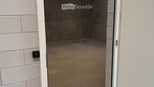 Empty garage with concrete floor, white brick walls, and an open door leading to a concrete-floored space.