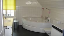Bathroom with a bathtub, toilet, sink, and a window with blinds. The room features white tiled walls and a black floor.