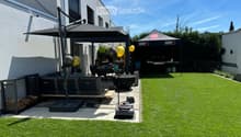 Well-maintained garden with artificial grass, patio seating area, umbrella, Weber grill, and balloons.
