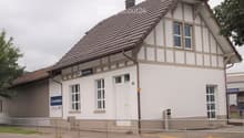 Two-story building with a tiled roof, white walls, and multiple windows. Features a sign reading "Gontenschwil" and a small entrance area with steps.