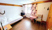 single bed, bedside table, TV, table, chair, window with curtains