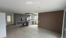 Modern kitchen and dining area with grey cabinets, a central island, a wooden dining table, and a sleek oven. The space features large windows and a contemporary design with a mix of wood and metal finishes.