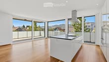 Modern kitchen with white island, wooden flooring, large windows offering a scenic view, and a range hood.