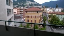 Balcony overlooking a city street with colorful buildings, parked cars, and distant mountains.