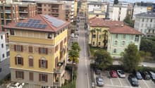 View from a balcony showing a street lined with buildings, parked cars, and a distant mountain range.
