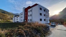 Modern multi-story building with white and red facade, located in a scenic mountainous area with a parking lot and surrounding greenery.