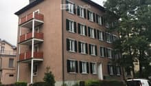 5-story building, red balconies, multiple windows, brown walls, entrance door, plant pots on balconies