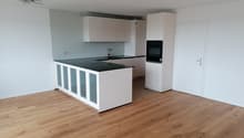 Modern kitchen with white cabinets, black countertop, and wooden flooring.