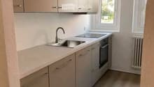 Modern kitchen with light grey cabinets, a double sink, and an oven. The space features light-colored countertops and a wooden floor.