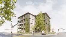 Modern multi-story building with a contemporary design, featuring large windows, balconies, and greenery integrated into the facade. The building is surrounded by trees and a paved area with a bench.