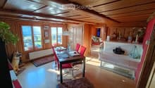 Cozy dining area with wooden ceiling, large windows, and a dog present. Includes a dining table with chairs, a lamp, and decorative items.