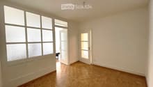 Empty room with wooden flooring, large frosted windows, and two open doors leading to other spaces.