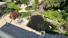 Well-maintained garden with a pond, seating area, and various plants and trees.