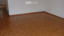 Empty room with wooden herringbone flooring and white walls, featuring a large white cabinet unit on one side and a visible doorway leading to another space.