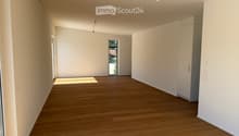 Empty room with wooden flooring, white walls, and built-in cabinets. Natural light streams in from a large window and a door leading outside.