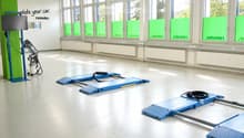 Empty room with large windows, white walls, and a smooth concrete floor. Contains blue ramps and a small machine on the left side.